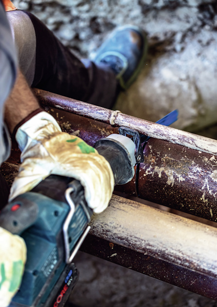 Person med skyddshandskar borrar ett rör med en bärbar borrmaskin.