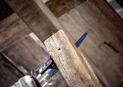 Närbild på en såg som skär igenom en träplanka, med sågspån som flyger omkring.