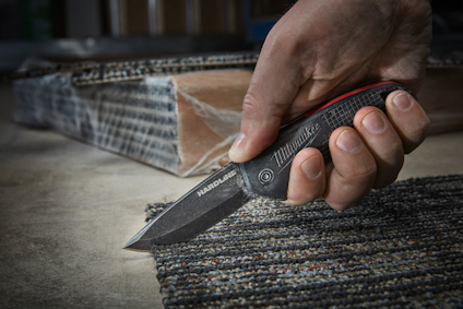 Person som håller i en kniv med texten "Hardware" på bladet, ovanpå en texturerad matta.