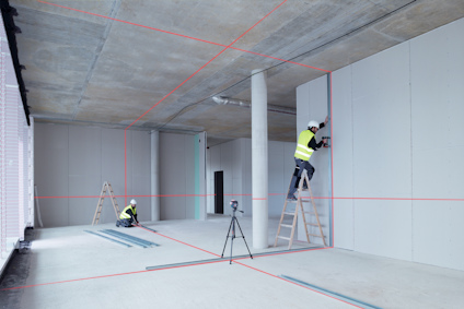 Två arbetare i byggarbetskläder, stegar och lasernivåer som projicerar röda linjer på väggar och tak.
