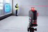 En arbetare med gul väst använder en enhet vid en vägg. En Bosch laseravsändare projicerar röda linjer.
