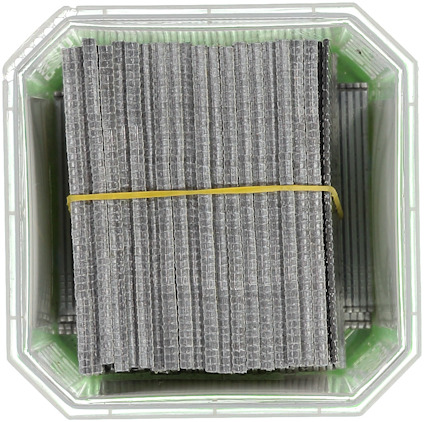 Staplar av metallspikar bundna med gummiband i en transparent behållare.